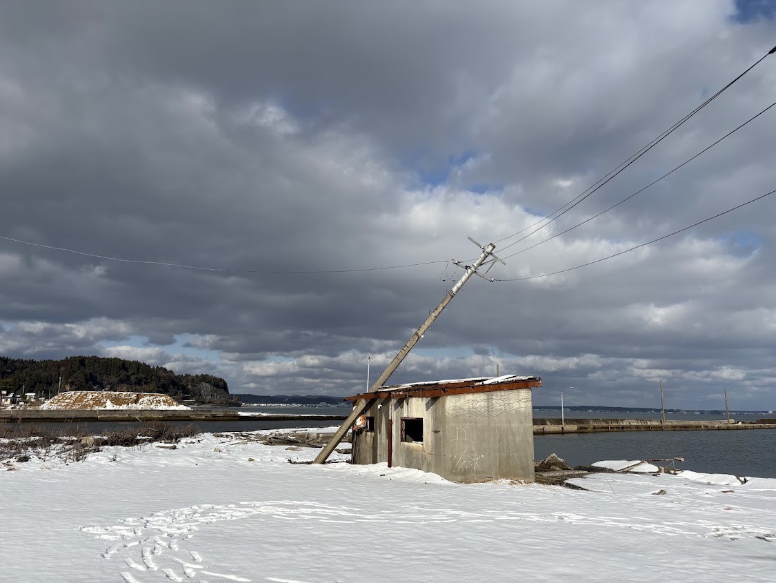 雪の積もる海辺と傾いた電柱
